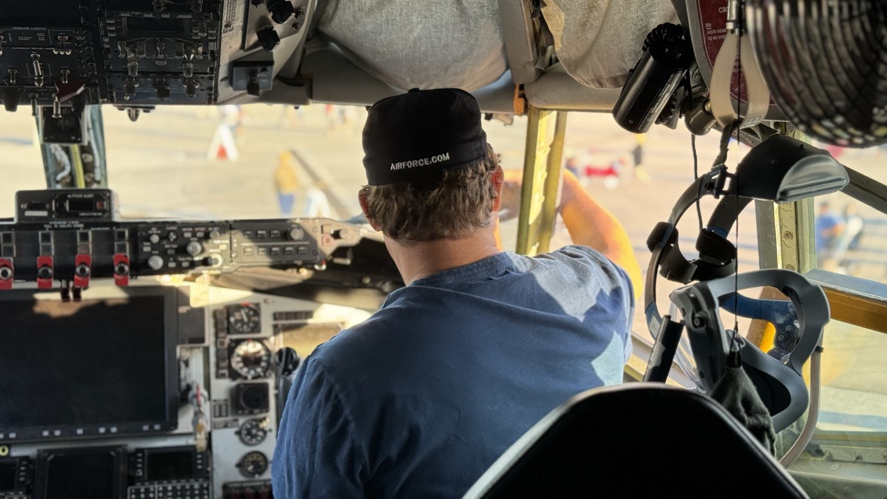 A man wearing a black hat and a blue shirt is in the cockpit of a plane.